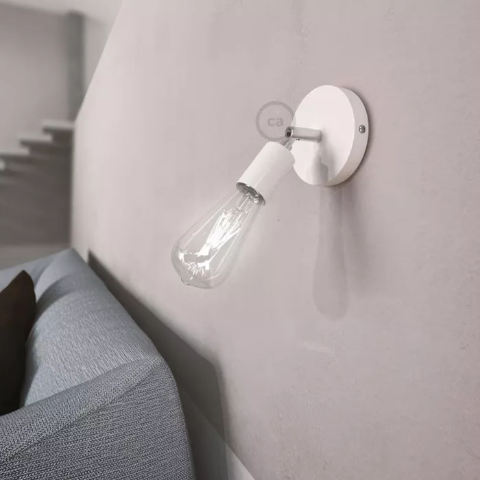 Darc — Une applique murale blanche fixée près d'un lit, avec une ampoule à vis transparente et un design épuré et moderne, éclairant légèrement la têt