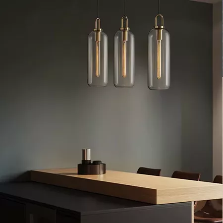 Darc — Trois appliques murales en verre transparent suspendues au-dessus d'un comptoir en bois clair, éclairées par des ampoules Edison à filament vis
