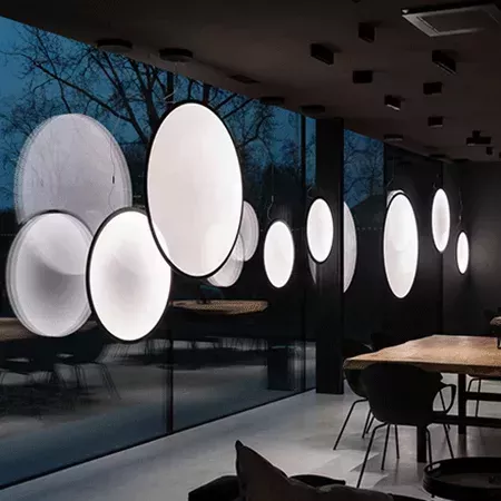 Darc — Une série de luminaires muraux circulaires blancs et noirs, suspendus en rangée devant une grande fenêtre offrant une vue sur un extérieur somb