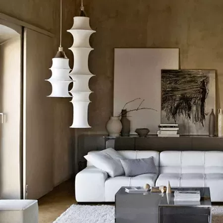 Darc — Deux appliques murales suspendues en forme de colonnes empilées et blanches, éclairant un salon contemporain avec un canapé blanc, une table ba