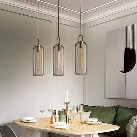 Darc — Trois appliques suspendues en verre fumé avec ampoules Edison au-dessus d'une table à manger en bois clair, entourée de chaises vertes et d'une