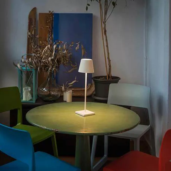 Darc — Une lampe blanche sur pied fine posée au centre d'une table ronde verte, entourée de quatre chaises colorées dans un espace lumineux et décoré