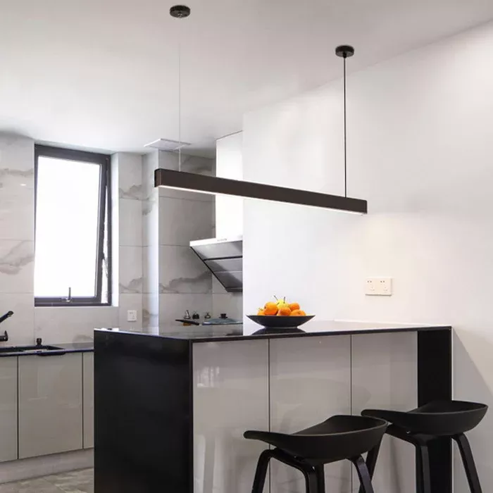 Darc — Une cuisine moderne avec un îlot central en plan de travail noir et carrelage blanc, éclairée par une lumière suspendue. On y voit deux taboure