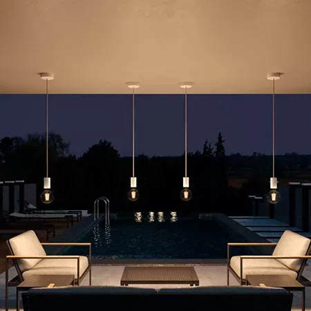 Darc — Une piscine rectangulaire éclairée par des lumières suspendues au-dessus, entourée de quatre fauteuils et d’une table basse en bois, dans un ca