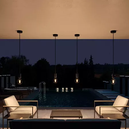 Darc — Un salon extérieur design avec deux fauteuils et une table basse en bois sombre, éclairé par quatre luminaires suspendus au-dessus d’une piscin