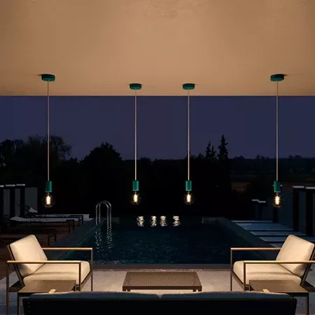 Darc — Une piscine extérieure rectangulaire entourée de quatre luminaires suspendus à ampoules visibles, éclairant un espace salon avec deux fauteuils