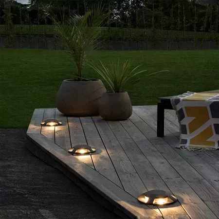 Darc — Terrasse en bois éclairée par trois lumières LED discrètes intégrées au sol, entourée de deux pots en terre cuite contenant des plantes vertes,
