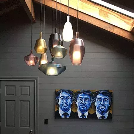 Darc — Une suspension composée de cinq luminaires en forme de gouttes aux reflets dorés et cuivrés, accrochée au plafond dans un espace sombre. À droi
