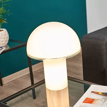 Darc — Une lampe design en forme de champignon blanc posée sur une table basse transparente, éclairée et entourée d’un espace salon moderne avec un ca
