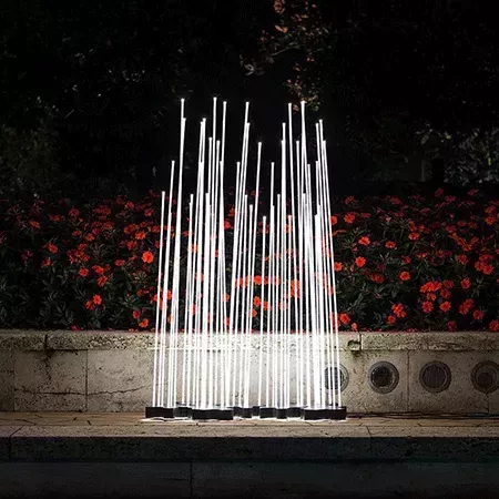 Darc — Installation lumineuse extérieure composée de plusieurs faisceaux lumineux blancs et fins, disposés en éventail, devant un mur végétalisé avec
