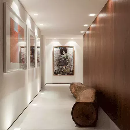 Darc — Un couloir étroit et lumineux aux murs blancs, décoré de trois cadres d’art contemporain aux couleurs vives et abstraites. À droite, un banc en