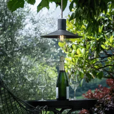 Darc — Une table extérieure en bois avec une bouteille de champagne et deux flûtes à vin posées dessus, éclairées par une lampe suspendue noire à ampo