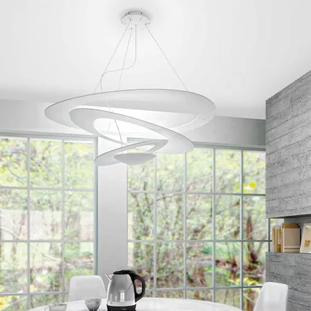 Darc — Une applique suspendue en forme de spirale blanche et élégante, fixée au plafond d'une cuisine lumineuse avec vue sur un jardin à travers de gr