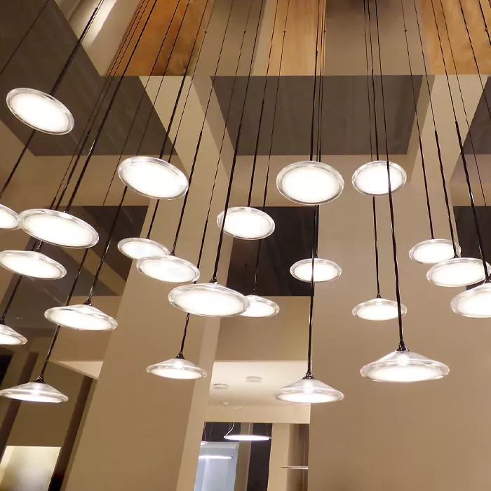 Darc — Ensemble de suspensions lumineuses rondes en verre suspendues par des fils noirs sous un plafond en bois clair et des poutres apparentes, créan