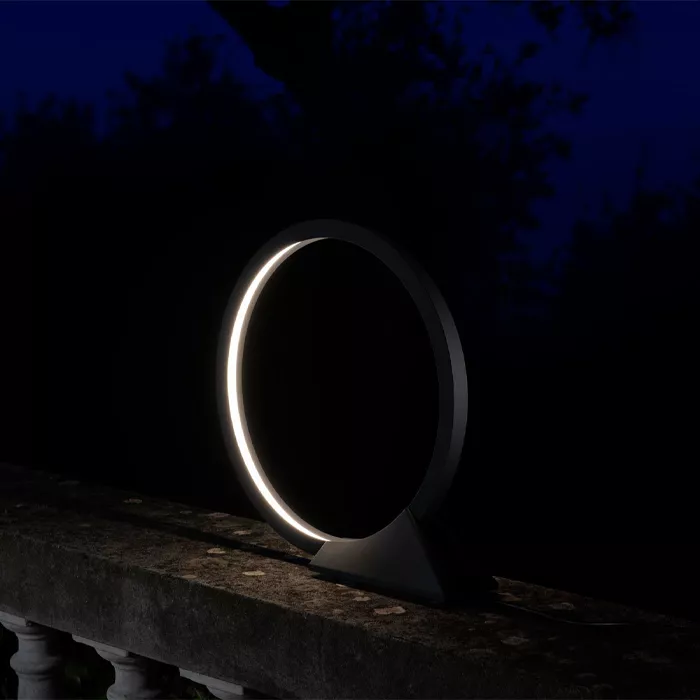 Darc — Un luminaire design en forme d'anneau lumineux posé sur une balustrade en pierre, éclairant faiblement une nuit étoilée.