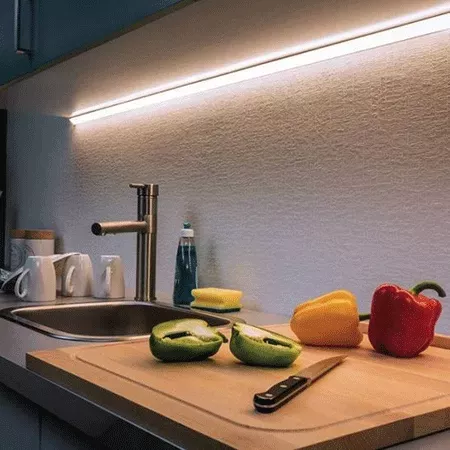 Darc — Une cuisine moderne avec un luminaire LED encastré sous les meubles, éclairant un plan de travail en bois clair. On y voit une bouteille d’eau,