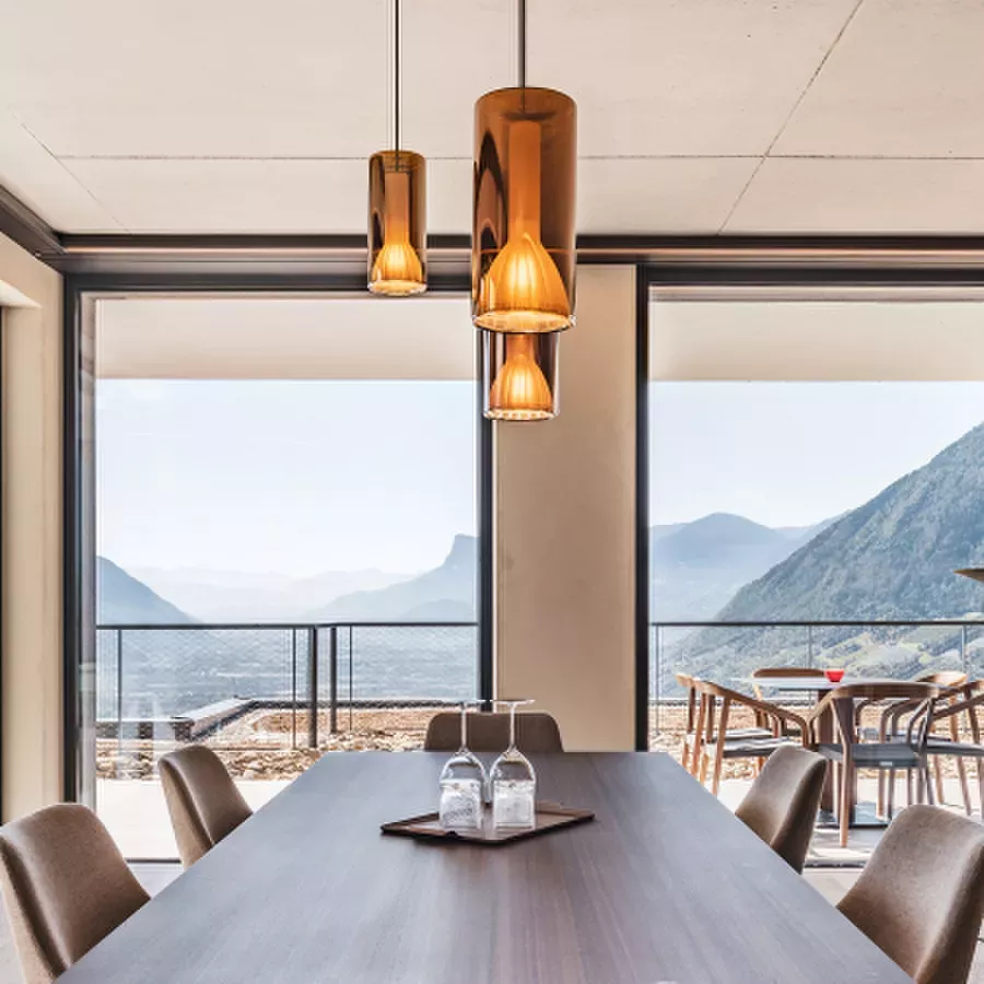 Darc — Une salle à manger moderne avec une grande table en bois centrale, deux chaises de chaque côté, des luminaires suspendus en métal doré et une v