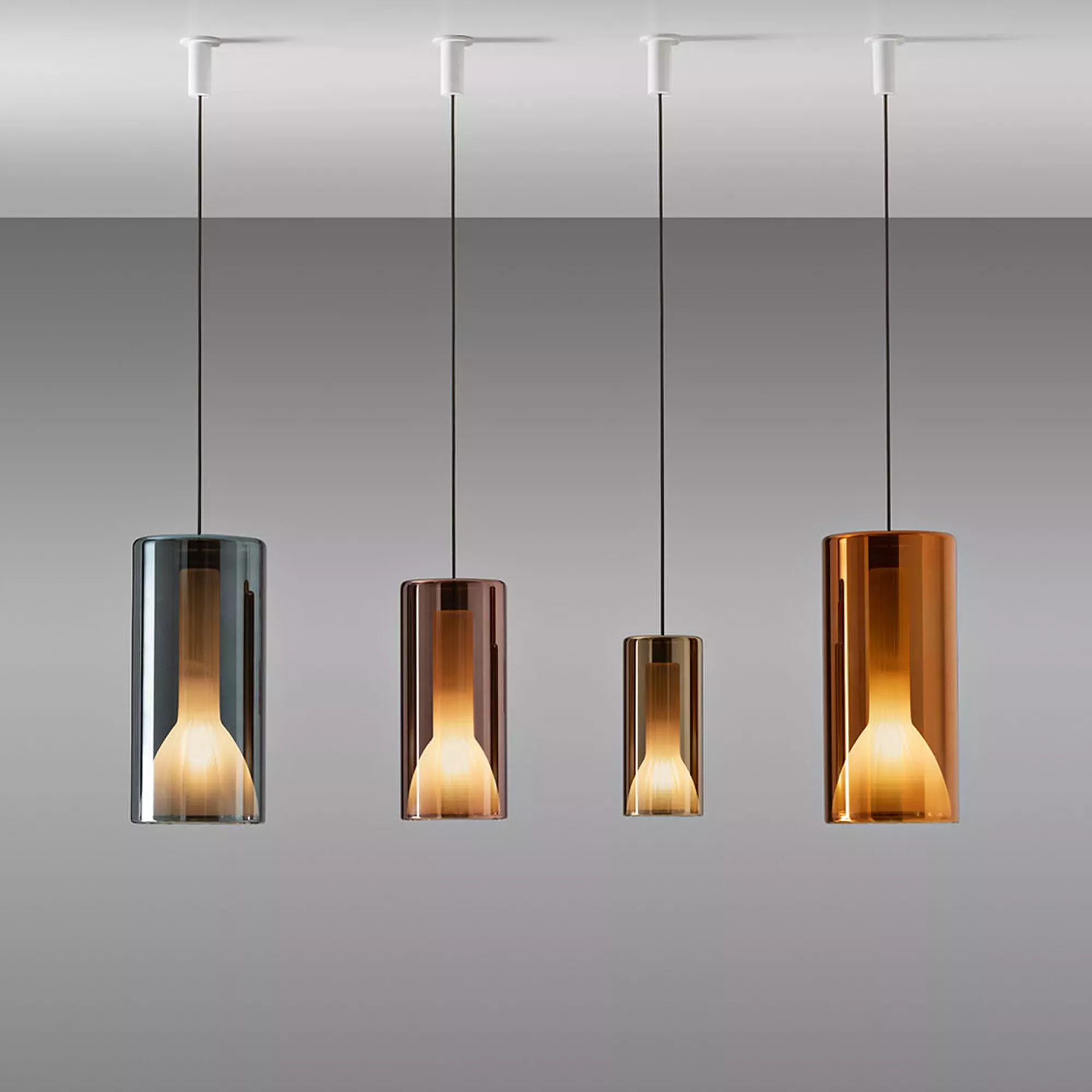 Darc — Quatre suspensions Penta Lit de design épuré, suspendues à des fils noirs, avec des abat-jour en verre transparent aux reflets bronze, cuivre e
