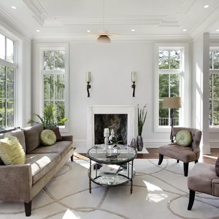 Darc — Un salon spacieux et lumineux avec un canapé en cuir beige, deux fauteuils assortis, une table basse en verre et métal au centre, une cheminée