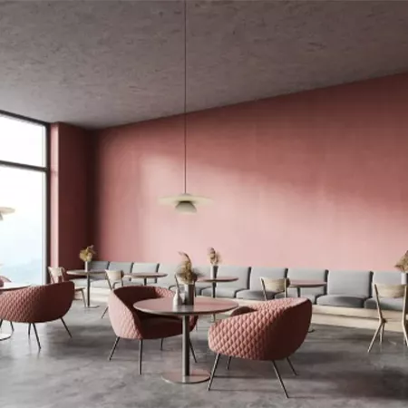Darc — Une pièce lumineuse aux murs peints en dégradé rose et gris, meublée de fauteuils en velours rouge et de tables basses noires, sous une suspens