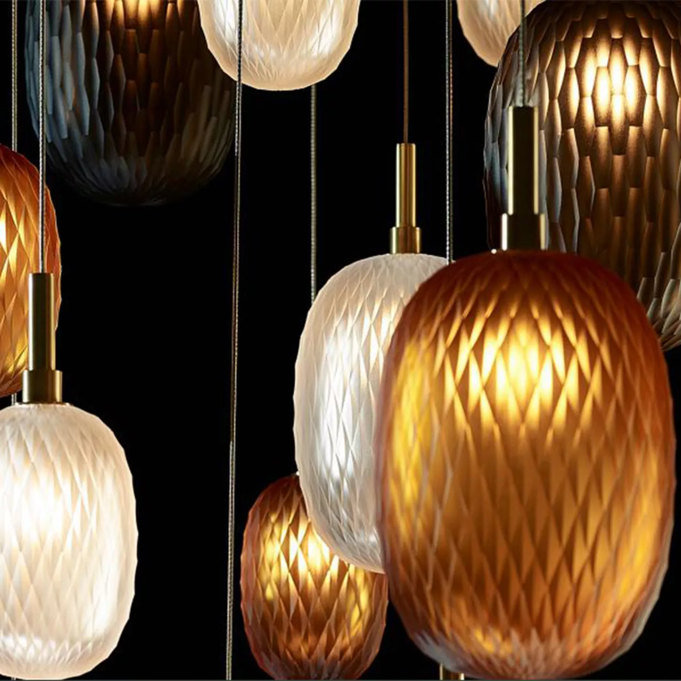 Darc — Une série de luminaires suspendus au design élégant, composés d'abat-jour en tissu de différentes teintes dorées et blanches, diffusant une lum