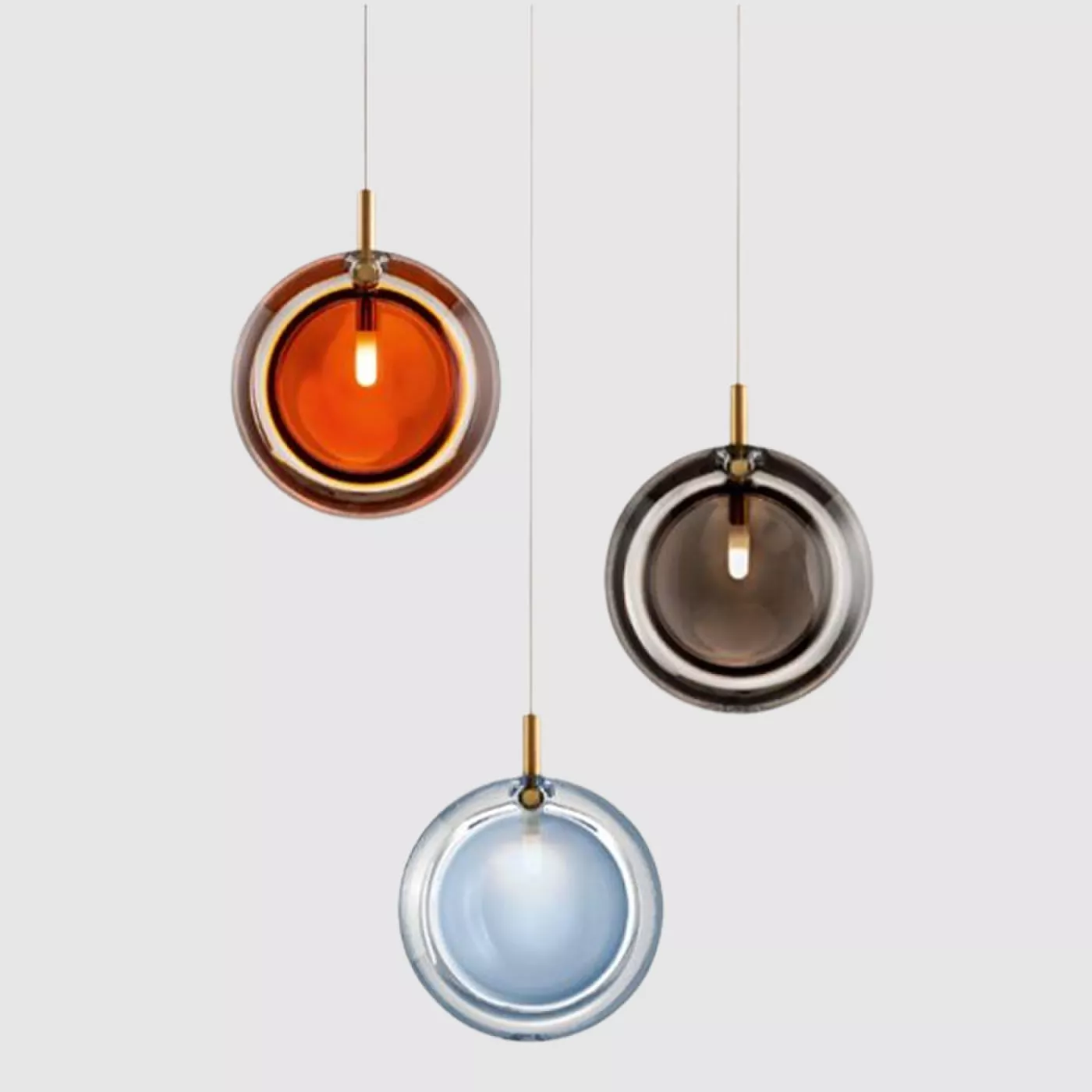 Darc — Trois suspensions lumineuses en forme de globes de verre suspendues par des fils métalliques dorés, émettant une lumière douce dans des tons am