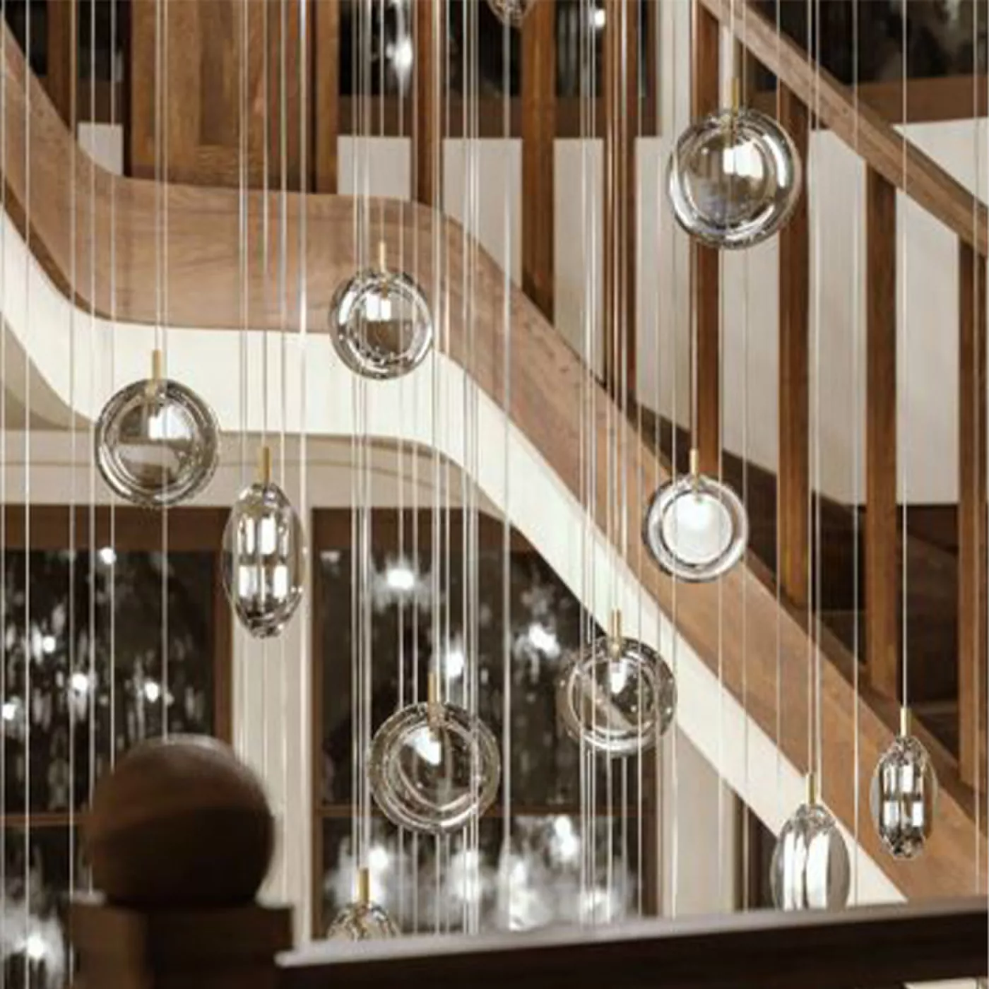 Darc — Une rampe d'escalier en bois clair avec des luminaires suspendus en métal et verre, composés de sphères et d’ampoules design, créant une ambian
