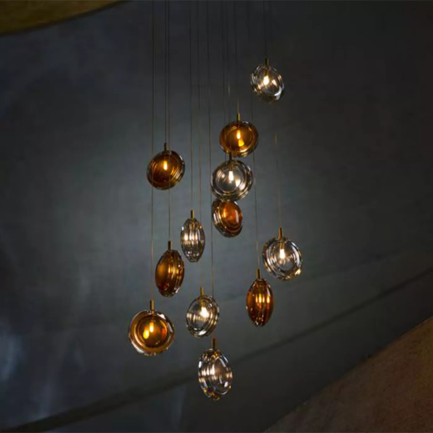 Darc — Ensemble de neuf lampes suspendues en forme de sphères translucides aux reflets dorés et argentés, disposées en cascade devant un mur gris clai