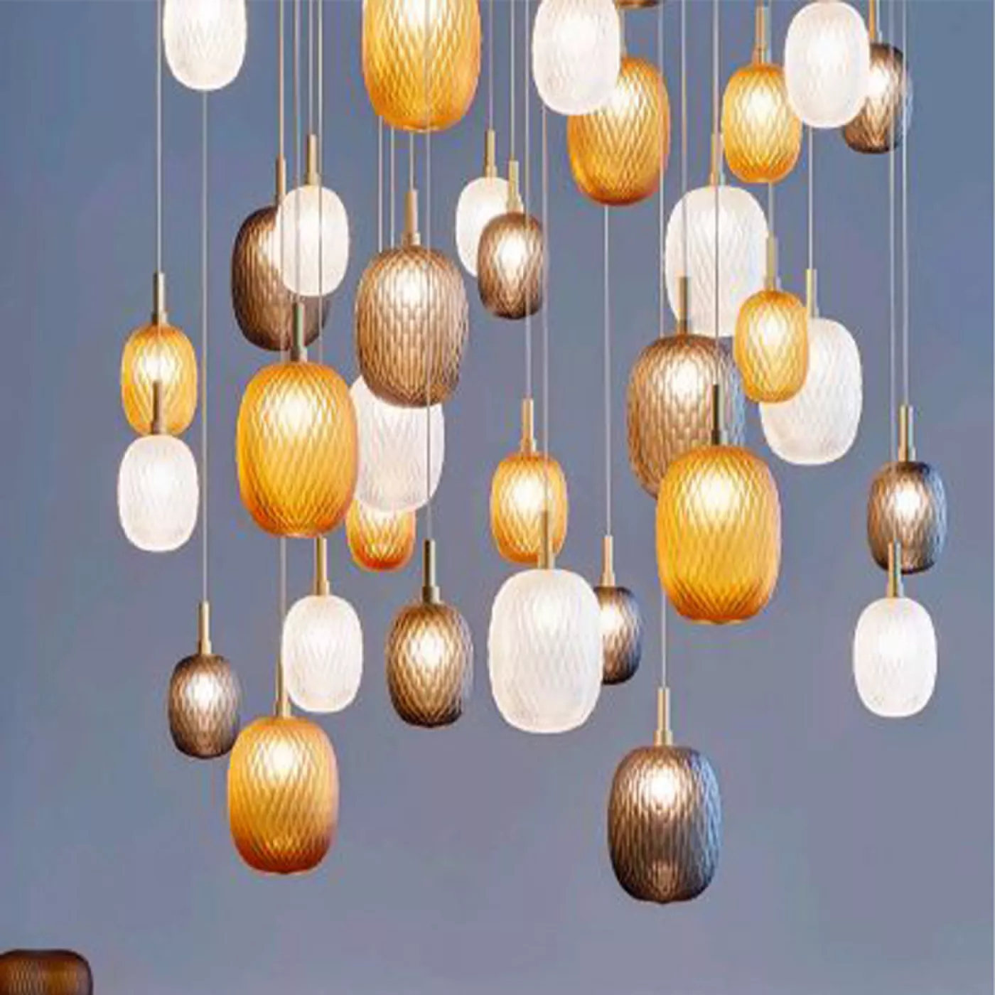 Darc — Une suspension lumineuse composée de multiples ampoules en forme d’amande, suspendues à différentes hauteurs, dans des tons dorés, cuivrés et b