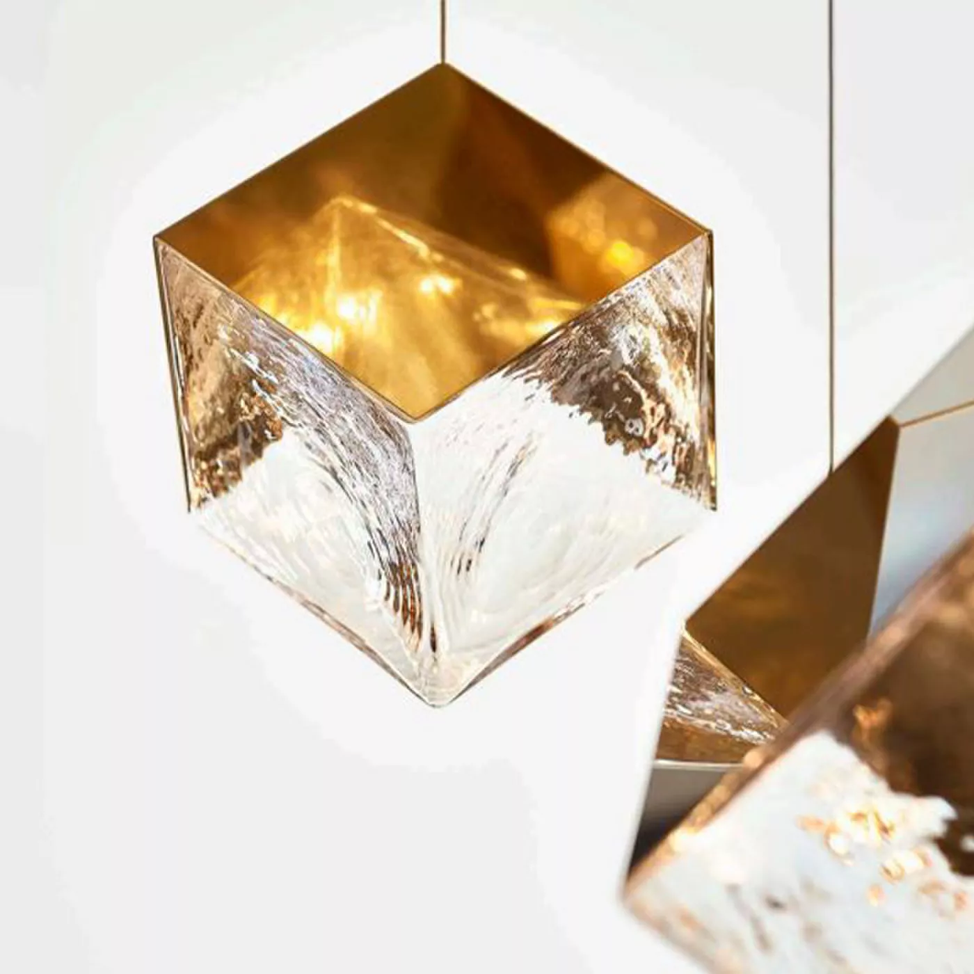 Darc — Un luminaire cubique suspendu au plafond, composé d’un cadre transparent texturé et d’un intérieur doré diffusant une lumière chaude et douce