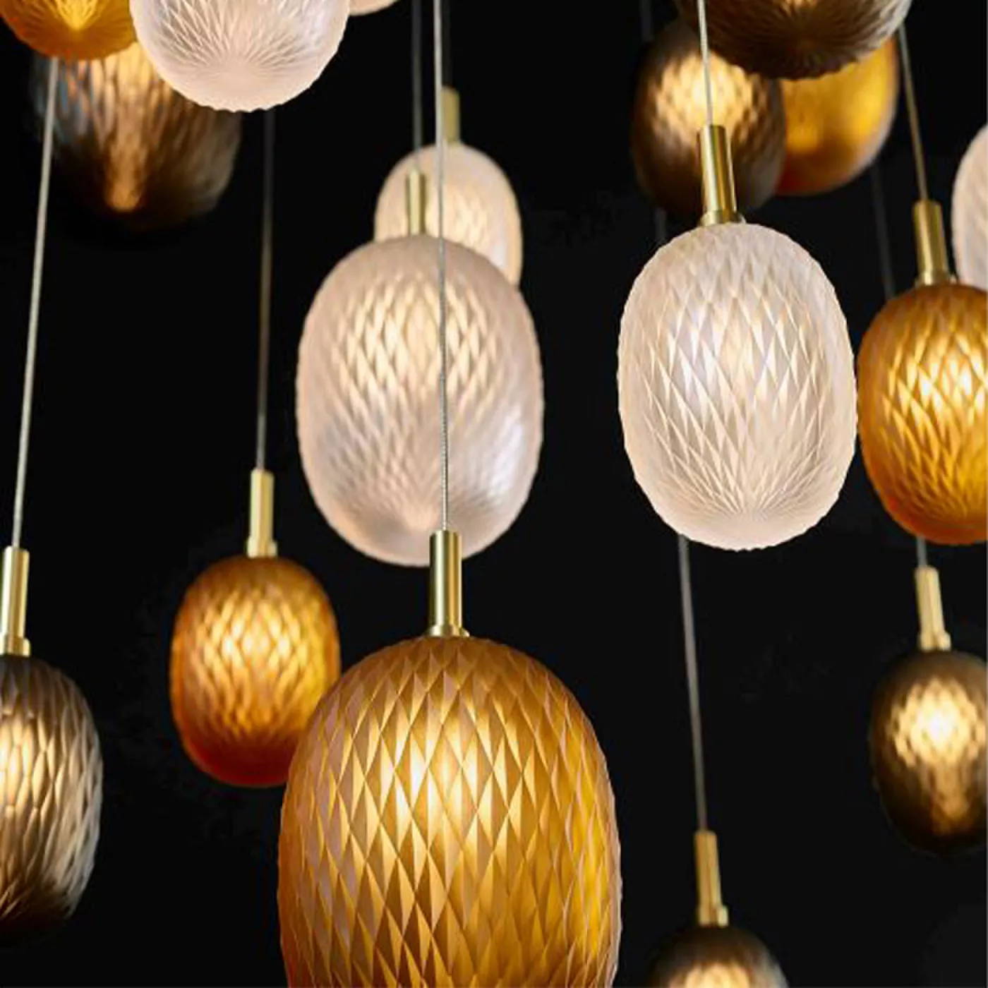 Darc — Une série de guirlandes lumineuses en forme d’œufs suspendues par des fils dorés, composées de sphères translucides dans des tons dorés et blan