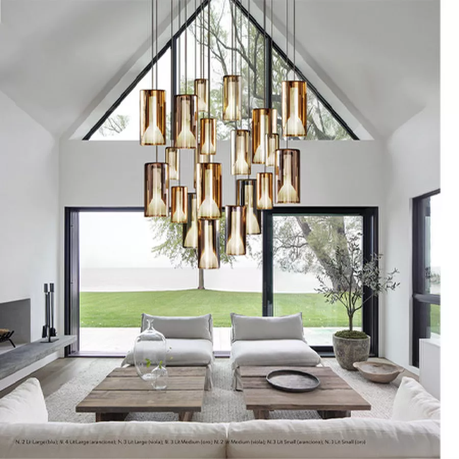 Darc — Un luminaire suspendu composé de plusieurs abat-jour dorés et transparents, accroché au plafond d'un salon spacieux avec vue sur un jardin verd