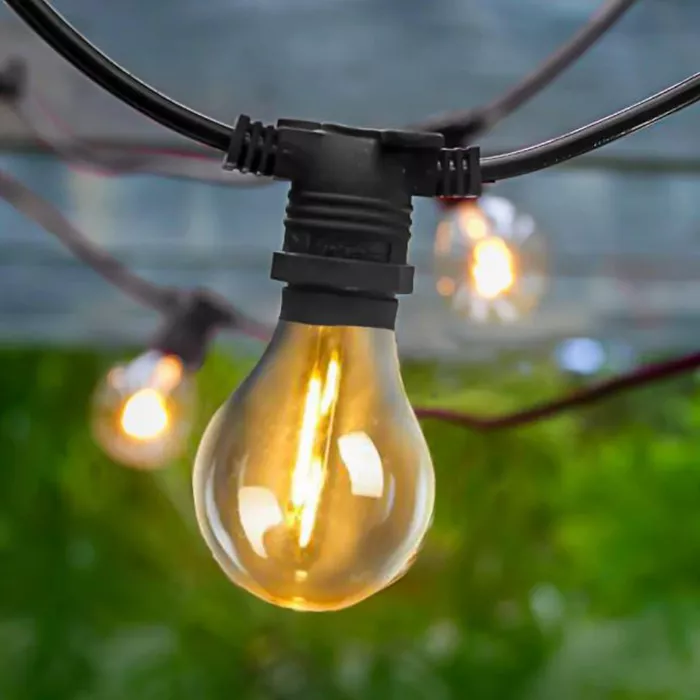 Darc — Une guirlande lumineuse suspendue composée d'ampoules en verre vintage de forme classique, diffusant une lumière chaude et dorée sur un fond de