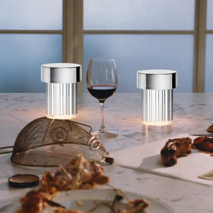 Darc — Deux luminaires design en métal argenté posés sur une table en marbre clair, encadrant un verre de vin rouge rempli à moitié et une assiette av