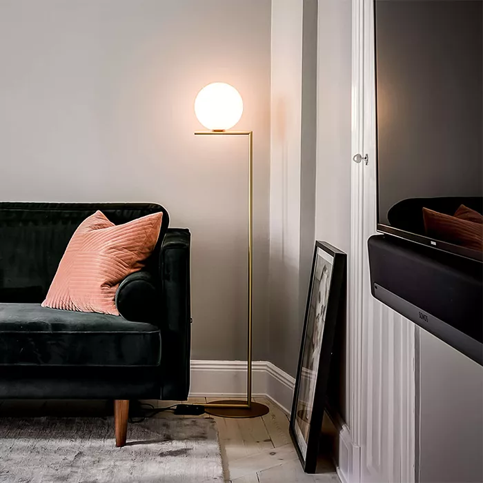 Darc — Un canapé noir profond avec un coussin rose en forme de losange posé sur l’accoudoir. À côté, une lampe murale design à globe blanc éclairant l
