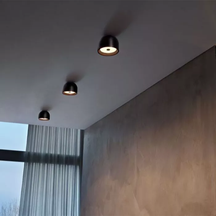 Darc — Trois spots encastrés dans un plafond bas, éclairant une surface murale en texture brute et lisse, avec une grande fenêtre voilée de rideaux gr