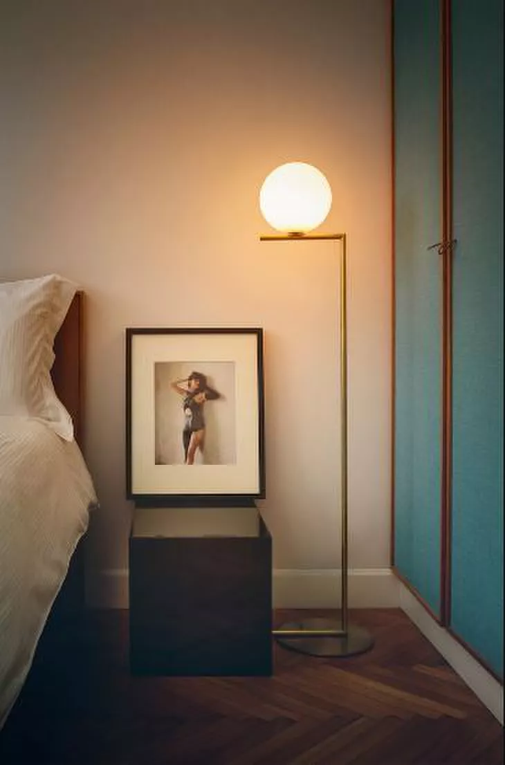 Darc — Une chambre sobre avec une lampe design à pied fin et globe lumineux blanc éclairant une photo encadrée d’une silhouette féminine en mouvement,