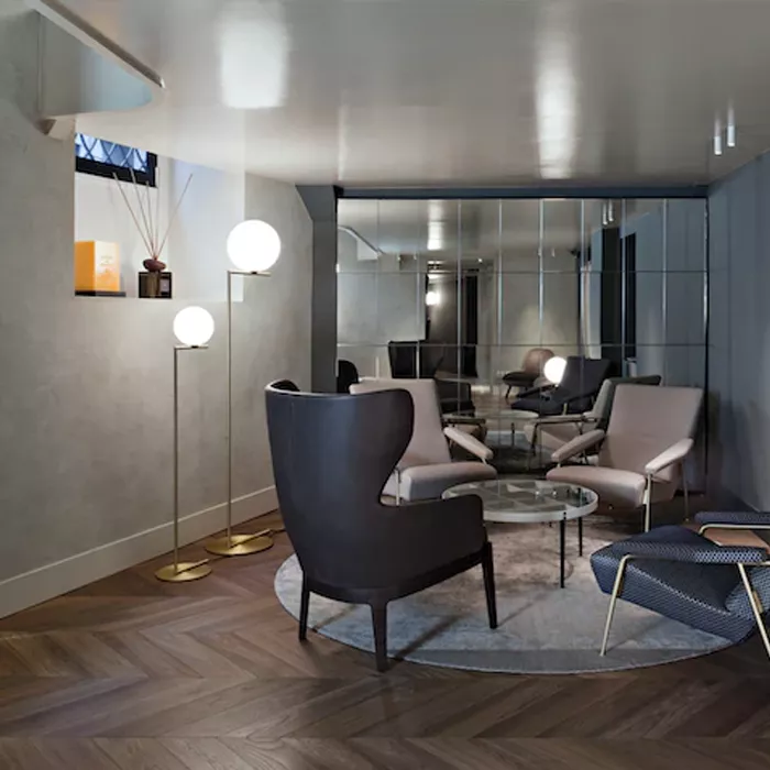 Darc — Un salon spacieux avec des fauteuils en cuir gris et beige disposés autour d’une table basse circulaire en verre. Deux lampes design à globes b