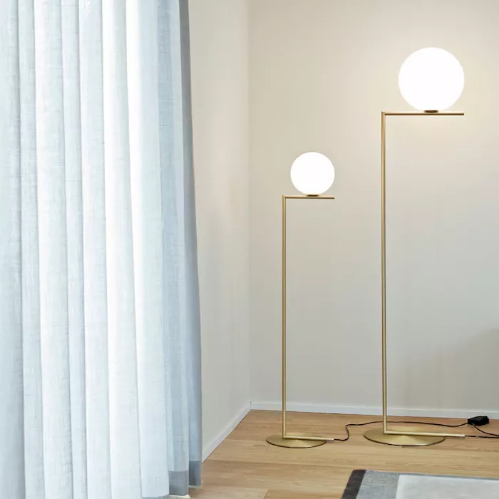 Darc — Deux appliques murales design en métal doré avec des globes lumineux blancs, placées près d’une fenêtre avec des rideaux gris clair, sur un sol