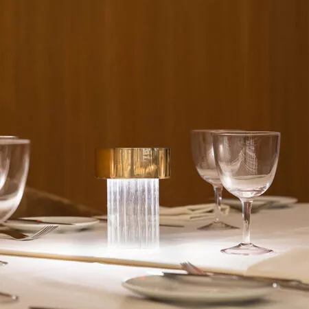 Darc — Une table finement dressée avec un bougeoir en métal doré et transparent au centre, entouré de verres à vin et couverts posés sur une nappe bla