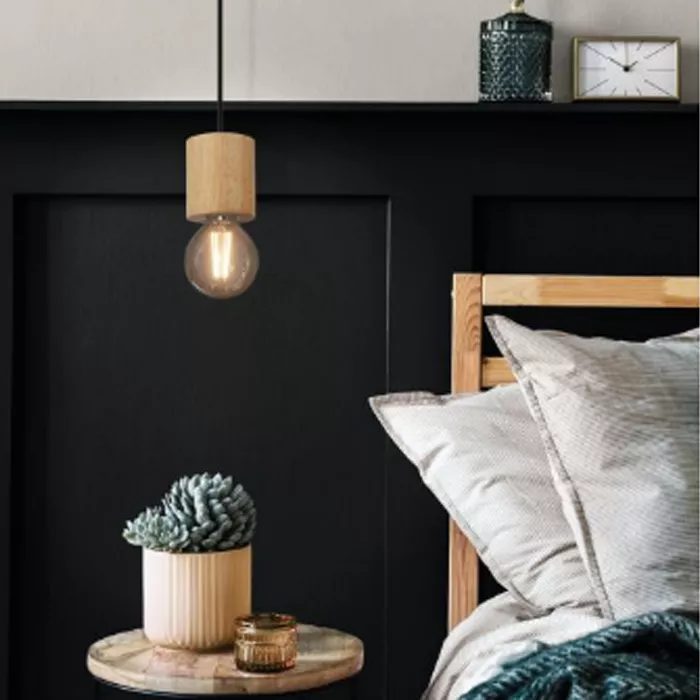 Darc — Une chambre épurée où une applique suspendue en bois naturel éclaire une tête de lit en bois clair. Sur une table basse ronde en bois, un pot e