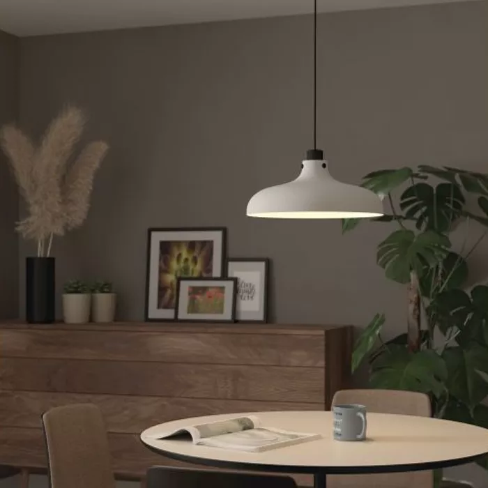 Darc — Une applique luminaire blanche en forme de cloche suspendue au plafond au-dessus d'une table ronde dans un salon moderne, entourée d'une plante