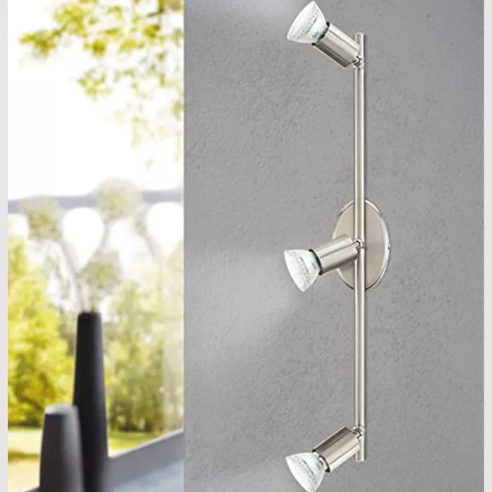 Darc — Deux appliques murales en métal chromé fixées sur un mur gris clair, chacune équipée de deux spots orientables avec ampoules visibles, éclairan
