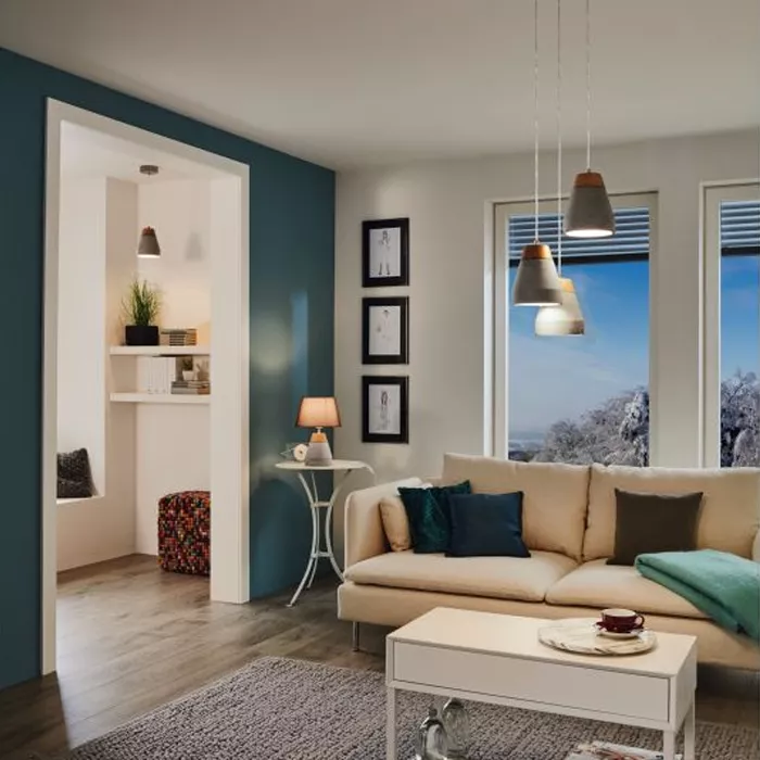 Darc — Un salon spacieux et lumineux où un canapé beige aux coussins bleus et verts est placé devant une grande fenêtre offrant une vue sur un paysage