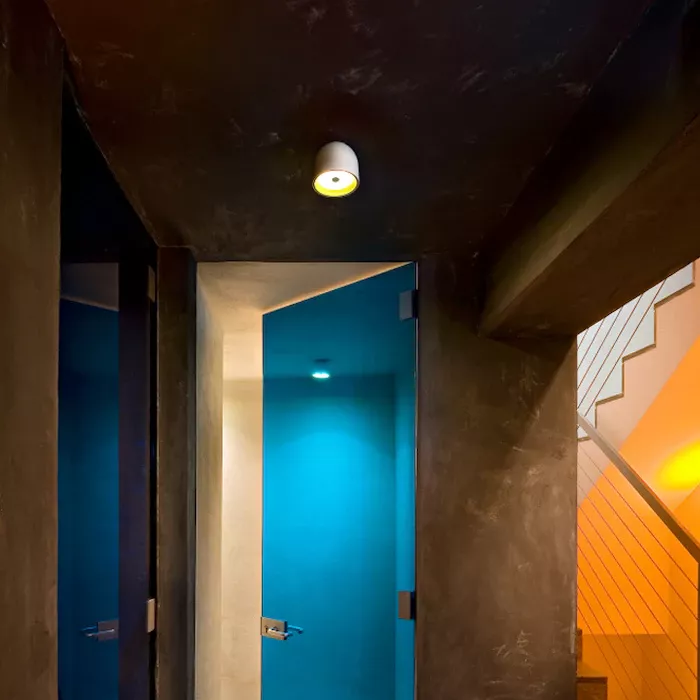 Darc — Deux portes murales bleues encastrées dans un couloir sombre éclairé par une lumière douce au plafond, avec un escalier en bois visible à droit