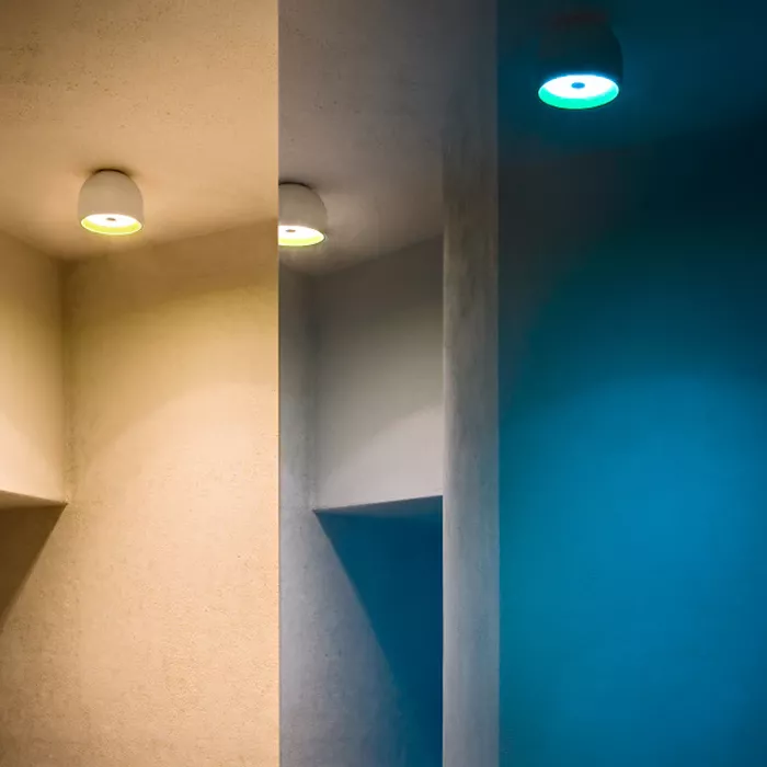 Darc — Un espace intérieur avec un mur miroir reflétant une lumière verte et bleue provenant de deux spots encastrés dans un plafond blanc, créant un