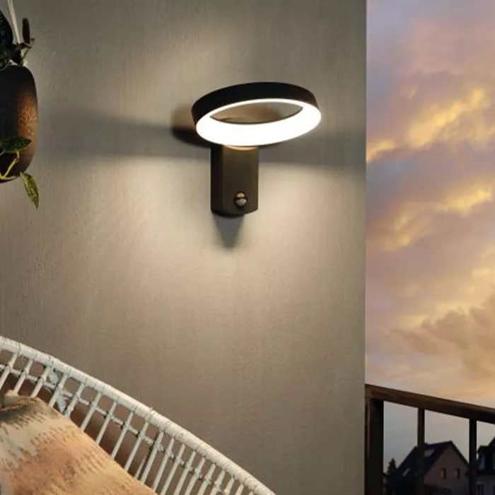 Darc — Une applique murale design en forme d'anneau lumineux fixée sur un mur clair, éclairant une tête de lit avec une couverture en lin, près d'une