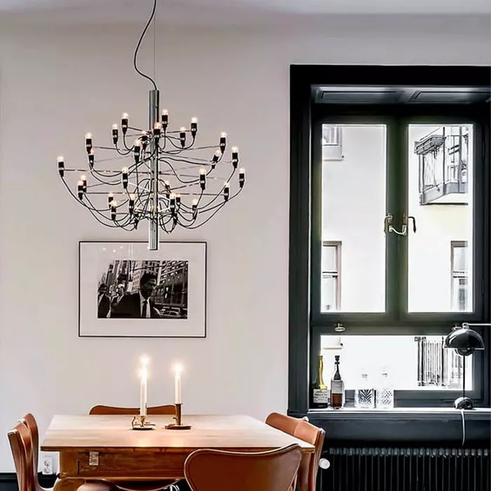 Darc — Un luminaire suspendu design en métal avec multiples branches et ampoules éclairant une table en bois clair entourée de chaises en cuir, près d