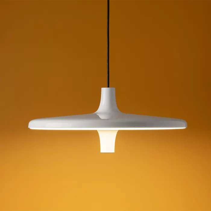 Darc — Applique murale suspendue en forme de disque plat et élancé, fixée par un câble noir, diffusant une lumière douce sur fond orange clair.