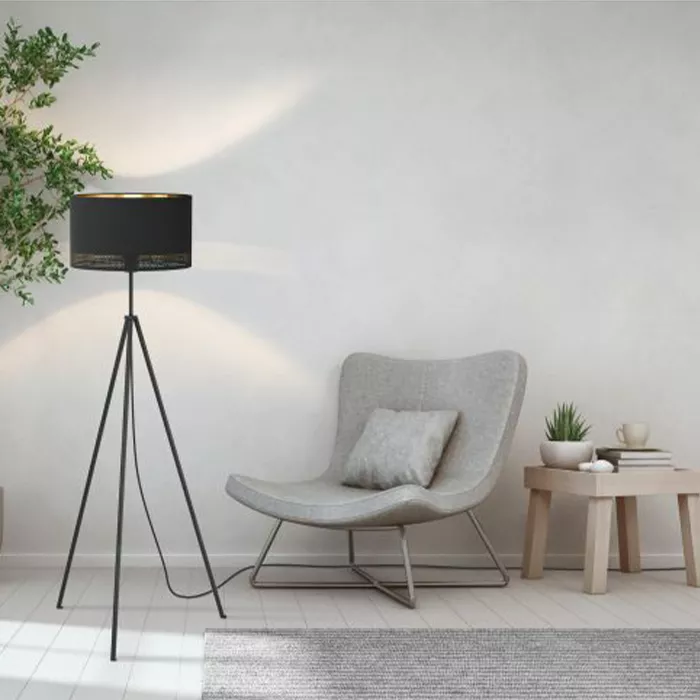 Darc — Une lampe sur pied noire en forme de cylindre avec une base tripode éclairant un fauteuil gris clair aux courbes douces, posé sur un tapis text